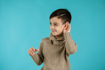 happy little child boy making hearing gesture on blue background. facial expression. kid with hand over ear listening gossip.