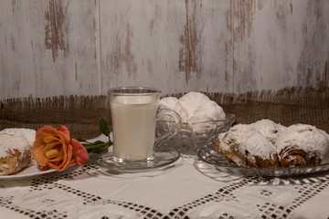 Close-up. On the table is a cup of milk. In the vases are marshmallows and croissants. Nearby lies a rose.