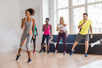 Beautiful african american trainer performing zumba movements with multicultural dancers in dance...