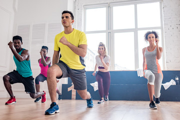 Low angle view of handsome trainer performing zumba with multiethnic dancers in dance studio