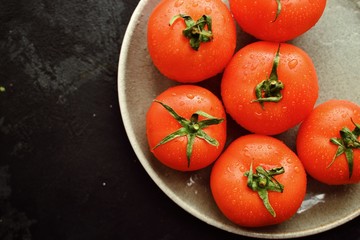 Ripe tomatoes in a gray clay bowl. Whole Tomatoes close-up on a concrete dark table background. Healthy raw vegetables.