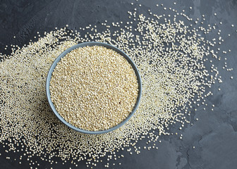 Dry quinoa seed grain in ceramic plate over black grange concrete background