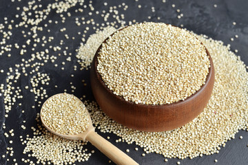 Raw organic quinoa grains in wooden bowl and spoon on dark stone background. Cooking ingredients, healthy food.