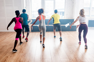 Back view of young multicultural dancers practicing zumba together in dance studio