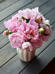 Bouquet of pink peony flowers in vase on wooden background