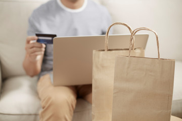 Man online shopping using laptop and credit card e wallet and paper bag foreground no plastic bag