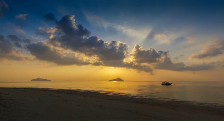 view panorama seaside of small boat floating in the sea with small island and sun rays with yellow sun light and cloudy sky background, sunrise at Ko Bulon Le, Stun Province, southern of Thailand.