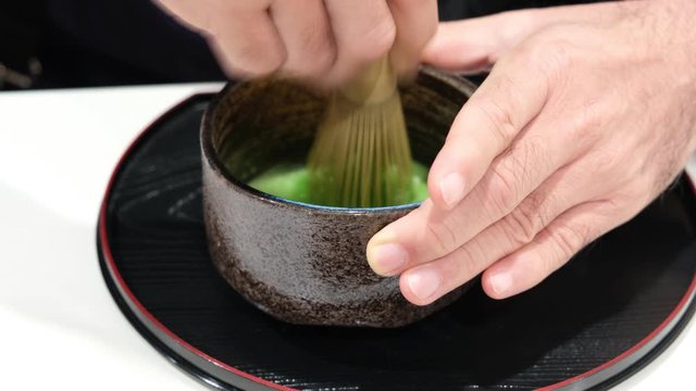 Male make japanese traditional hot macha green tea in ceramic cup. Left hand catch ceramic pot right hand whisk bamboo tool in water.