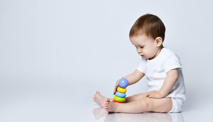 Newborn baby boy toddler playing with a multi-colored developing pyramid it on a gray with copy space