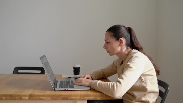 Young woman sitting at the table and working on laptop with bad posture. Health problem. Scoliosis