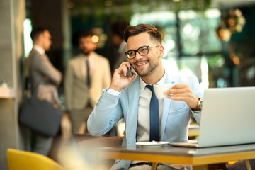 Young business man talking mobile phone and drinking coffee