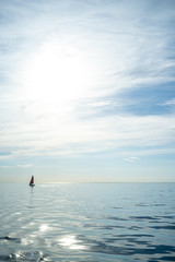 Naklejka premium Wonderful summer landscape. Sailboat in the sea on the horizon against the blue sky with clouds and the sun. Active holidays.