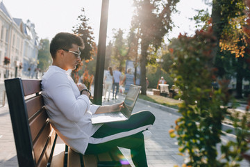 young stylish guy in shirt with phone and notebook on bench on sunny warm day outdoors, freelance