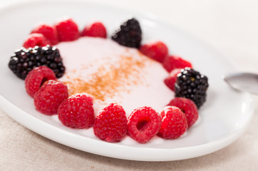 raspberries and blackberries laid out on a white plate in circle with yogurt and cinnamon
