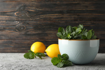Bowl with mint and lemons on grey background, space for text