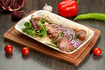 Barbecue on a white plate and a wooden cutting Board with sauce and onions