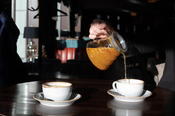 Woman is pouring sea buckthorn tea into a cup in a cafe