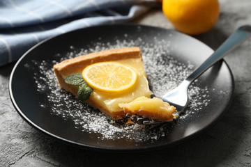 Plate with lemon tart slice on grey background with towel and lemon, close up