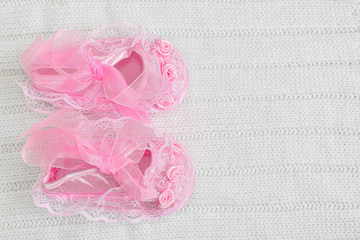 Pink baby booties from above on white crochet blanket. Shoes with lace, shiny ribbon and silk rose decoration. Copy space right.