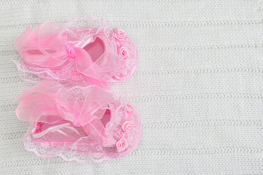 Pink Baby Booties From Above On White Crochet Blanket. Shoes With Lace, Shiny Ribbon And Silk Rose Decoration. Copy Space Right.