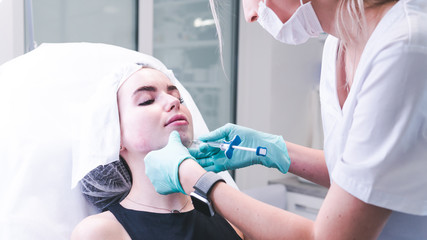 The female beautician doctor making injection in young woman face. The doctor cosmetologist doing facial contouring procedure.