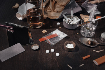 Various drugs, alcohol and cigarettes are on the wooden table. Substances that cause drug and alcohol dependence. Low key.