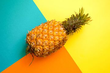 Ripe pineapple on a geometric pattern yellow, orange and cyan colour background. Flat lay