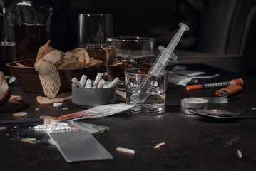 Various drugs, alcohol and cigarettes are on the wooden table. Substances that cause drug and alcohol dependence. Low key.