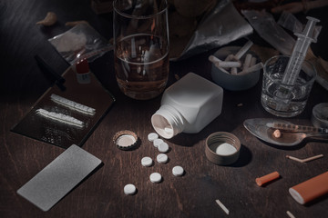 Various drugs, alcohol and cigarettes are on the wooden table. Substances that cause drug and alcohol dependence. Low key.