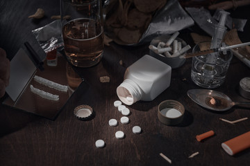 Various drugs, alcohol and cigarettes are on the wooden table. Substances that cause drug and alcohol dependence. Low key.