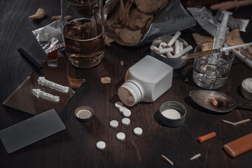 Various drugs, alcohol and cigarettes are on the wooden table. Substances that cause drug and alcohol dependence. Low key.