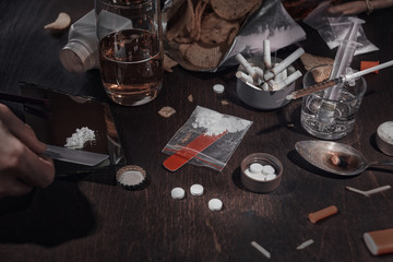 Various drugs, alcohol and cigarettes are on the wooden table. Substances that cause drug and alcohol dependence. Low key.
