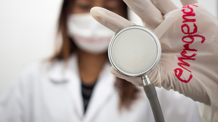 Female doctor wear white glove have text "emergency"  and wear a mask   and holding  Medical stethoscope . Concept  World Health Organization (WHO) Emergency declaration of corona virus .
