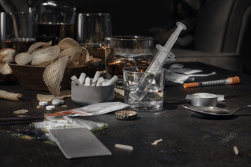 Various drugs, alcohol and cigarettes are on the wooden table. Substances that cause drug and alcohol dependence. Low key.