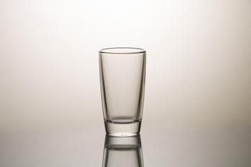 Empty glass on a reflective surface on a background with a gradient