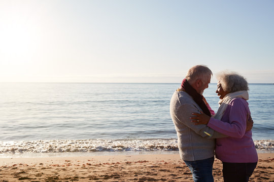 Profile View Of Loving Retired Couple Hugging Standing By Sea On Winter Beach Vacation