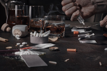 Various drugs, alcohol and cigarettes are on the wooden table. Substances that cause drug and alcohol dependence. Low key.