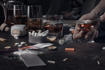 Fototapeta na wymiar Various drugs, alcohol and cigarettes are on the wooden table. Substances that cause drug and alcohol dependence. Low key.