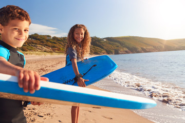 Portrait Of Children Wearing Wetsuits Carrying Bodyboards On Summer Beach Vacation Having Fun By Sea