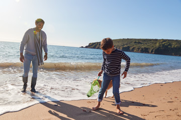 Father And Son With Dog Walking Along Beach By Breaking Waves On Beach Holding Fishing Net