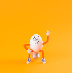 Winking Easter egg toy in the shape of a light bulb on a yellow - 319719386