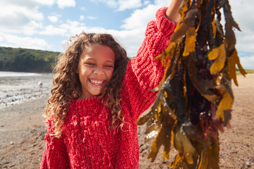 Portrait Of Smiling Girl Holding Seaweed On Winter Beach Vacation © Monkey Business