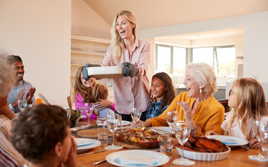 Mother Serving Food As Multi-Generation Family Meet For Meal At Home