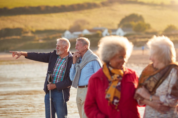 Group Of Smiling Senior Friends Walking Arm In Arm Along Shoreline Of Winter Beach