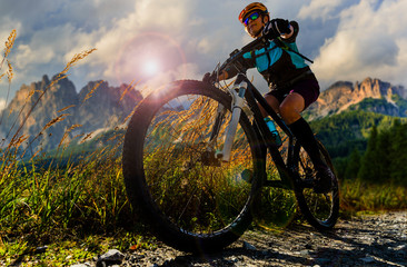 Tourist cycling in Cortina d'Ampezzo, stunning rocky mountains on the background. Woman riding MTB enduro flow trail. South Tyrol province of Italy, Dolomites. - obrazy, fototapety, plakaty