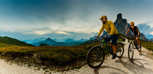 Naklejka na ściany i meble Cycling woman and man riding on bikes in Dolomites mountains andscape. Couple cycling MTB enduro trail track. Outdoor sport activity.