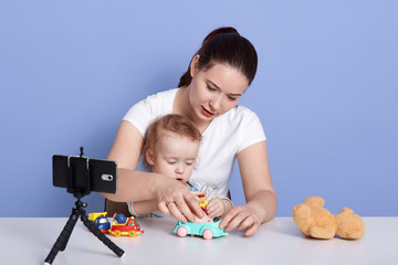 Image of beautiful young mother playing with her little son, mommy and infant play with toy car and filming video for her vlog, mum making content for her vlog about childre. Technology concept.