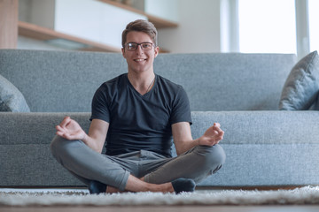 casual guy sitting in Lotus position on carpet in his living room