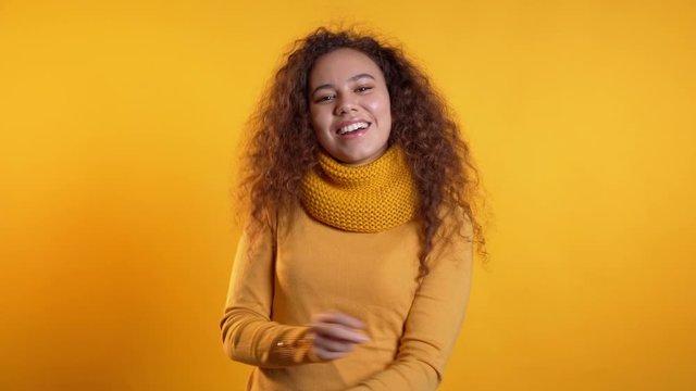 Beautiful woman with curly hair dancing with hands on yellow studio background. Cute girls portrait. Party, happiness, freedom, youth concept.