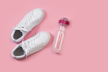 Zapatillas blancas junto a una botella de plástico sobre un fondo rosa liso y aislado. Vista...